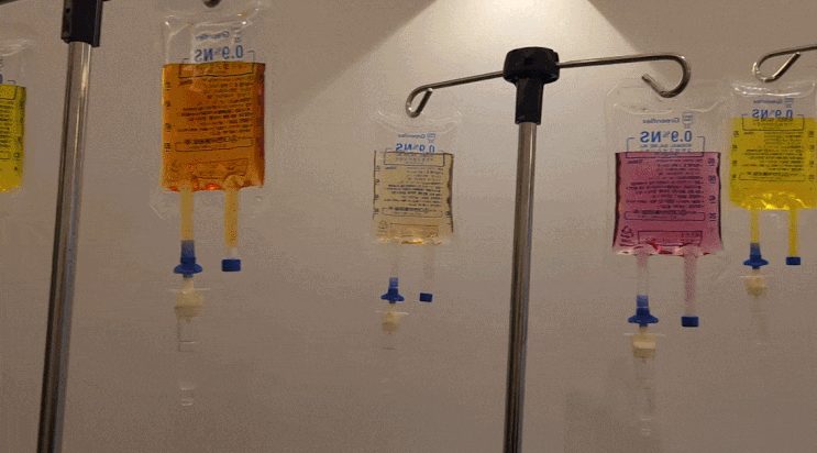Several IV bags of different colors hanging in a treatment room