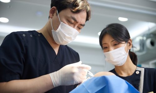 마스크와 장갑을 착용한 의료진이 보조 인력과 함께 파란 시술포를 덮은 환자에게 시술하는 장면